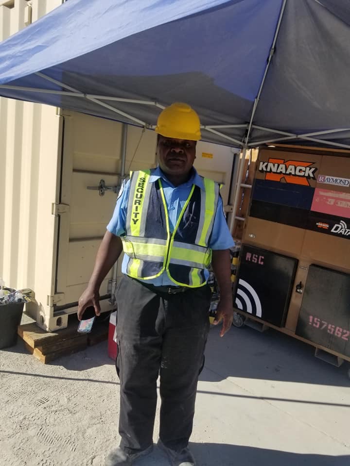 A man in safety gear standing under an umbrella.