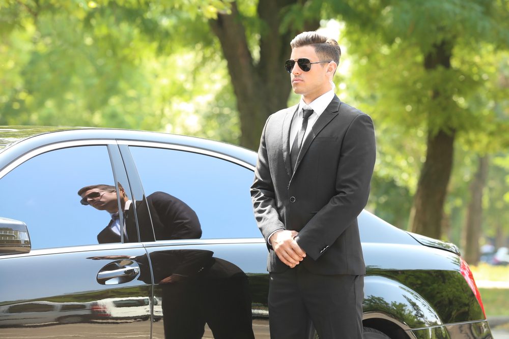 A man in suit and tie standing next to a car.